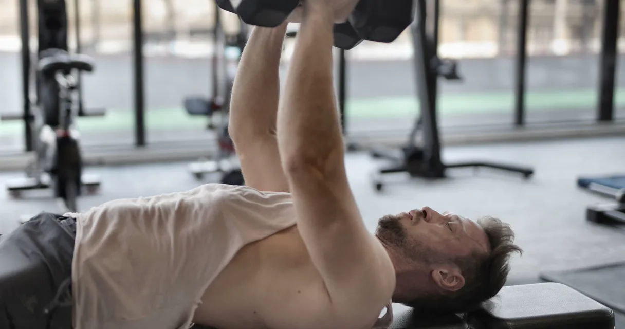 Athlete performing a dumbbell pullover on a flat bench in a gym