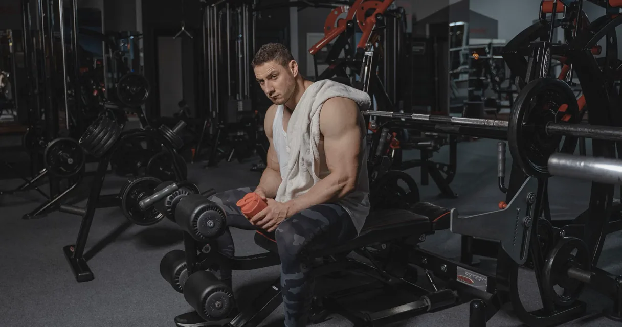 Athlete resting between barbell training sets in a gym